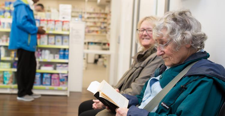 Two elderly women sitting in a pharmacy waiting for their prescription