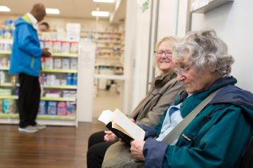 Two elderly women sitting in a pharmacy waiting for their prescription